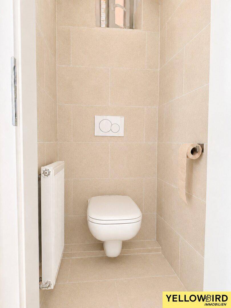 Separates WC mit wandhängender Toilette und beigefarbenen Fliesen, sauber und funktional.