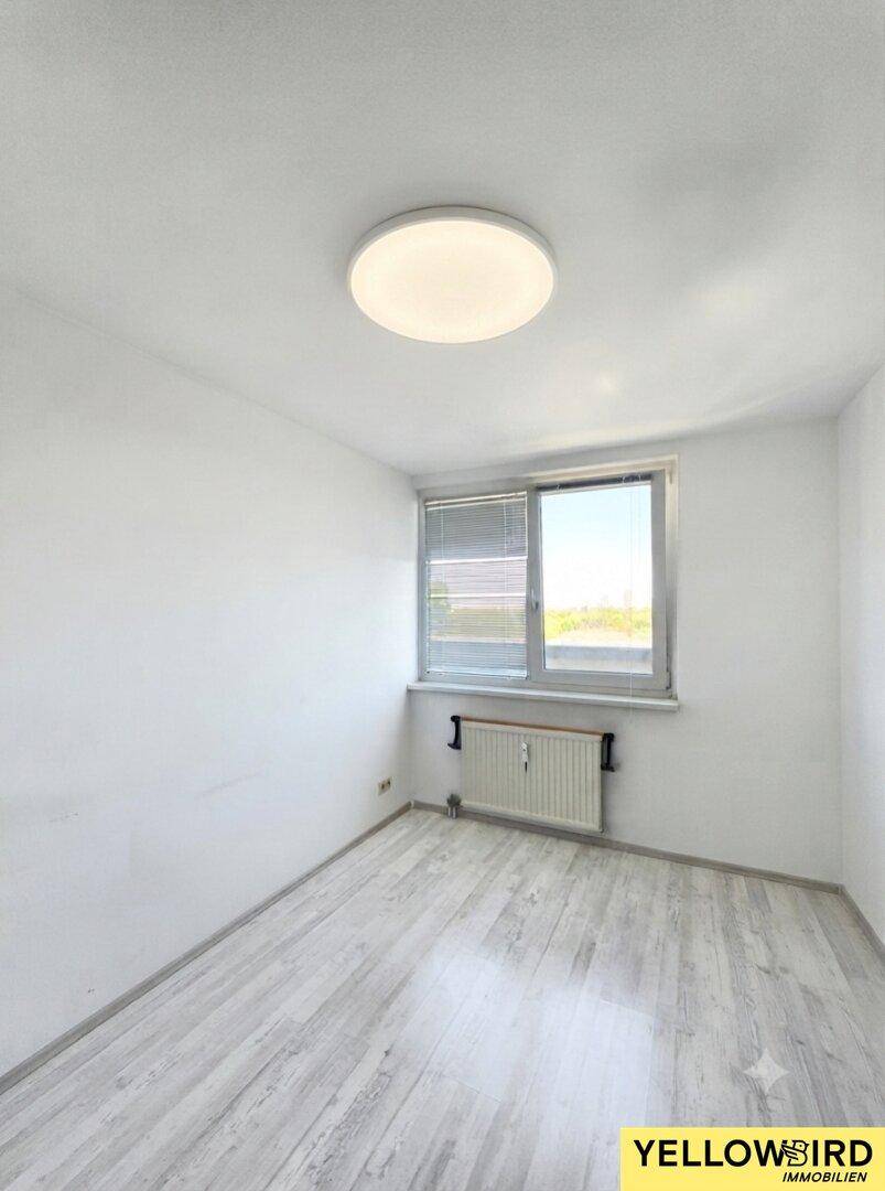 Helles, unmöbliertes Zimmer mit Laminatboden, Fenster und Heizkörper.