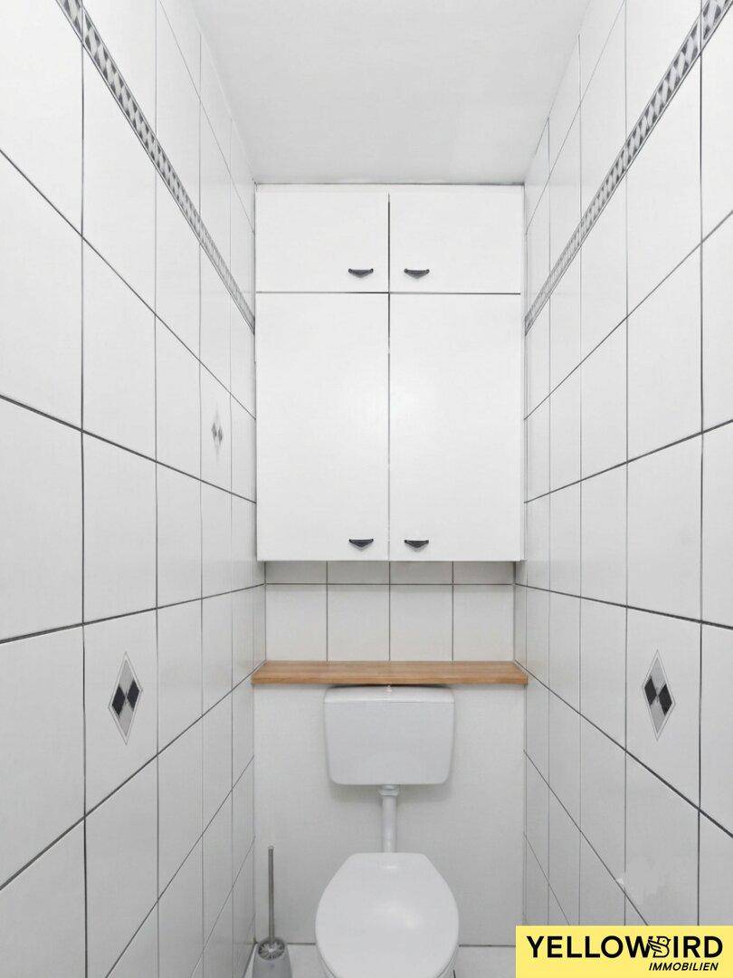 Kleines WC mit weißen Fliesen, Toilette und praktischen Wandschränken.
