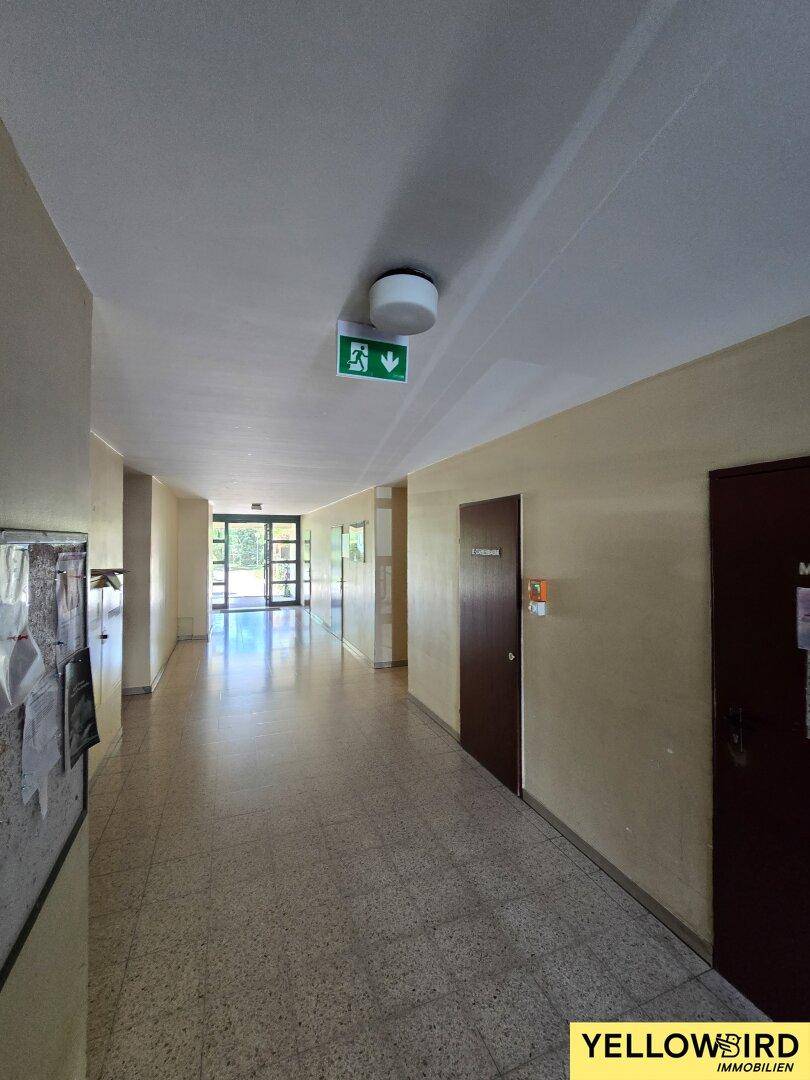 Langer, heller Flur im Gebäude mit Terrazzoboden und mehreren Türen.