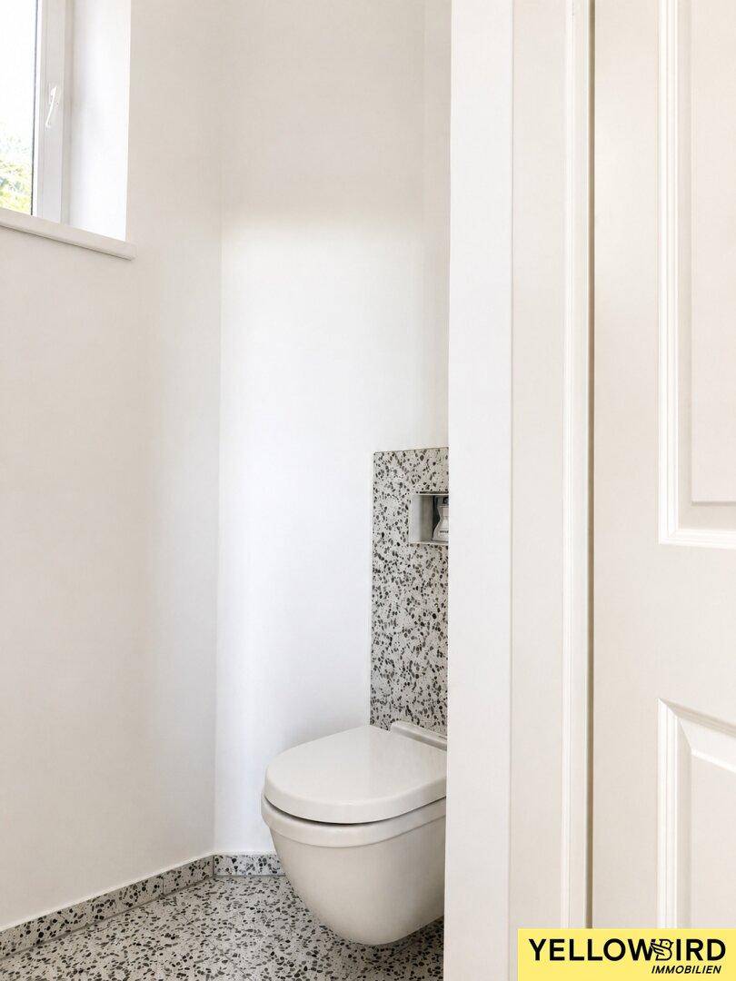 Modernes Gäste-WC mit wandhängender Toilette und kleinen grauen Fliesen.