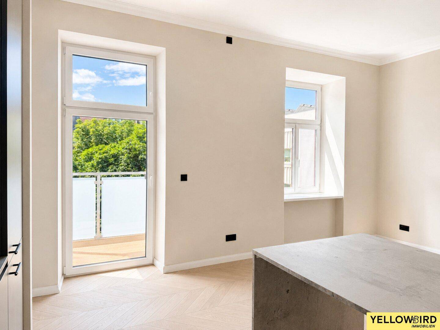 Heller Wohnbereich mit Zugang zu einem Balkon und großen Fenstern, die viel Tageslicht hereinlassen.