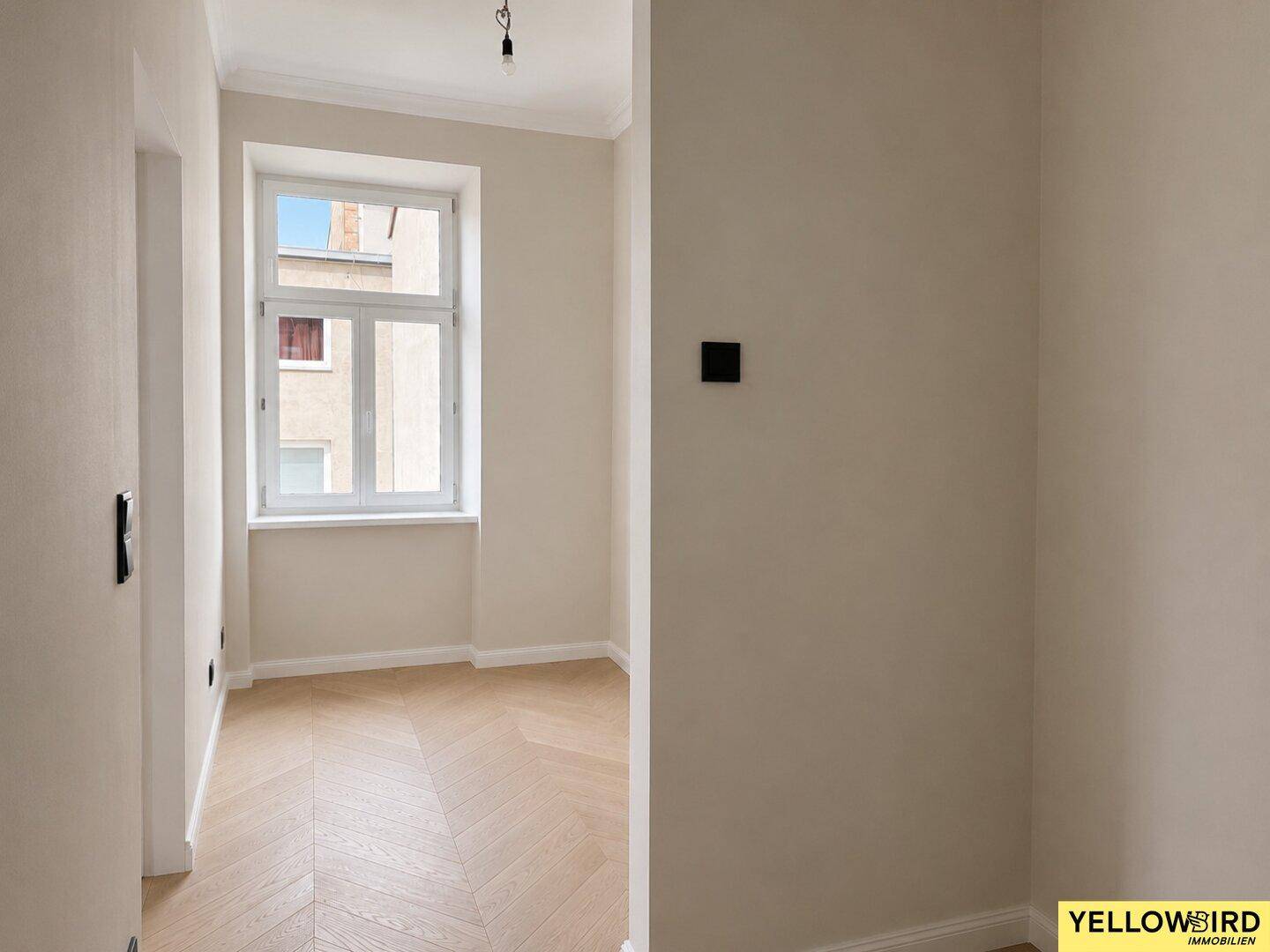 Heller Flur mit Fischgrätparkett und einem Fenster, das Tageslicht in den Raum bringt.