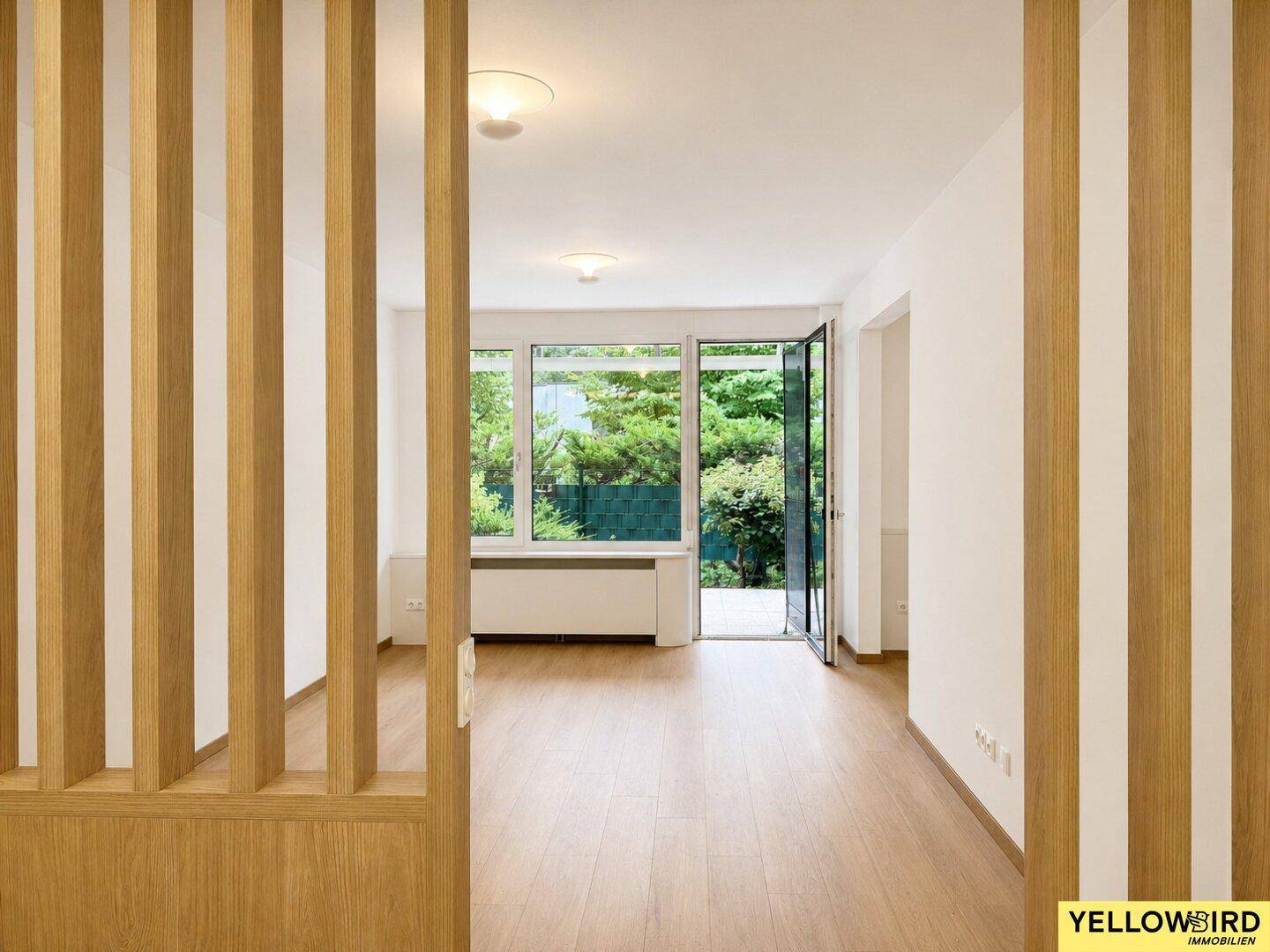 Lichtdurchfluteter Wohnbereich mit großen Fenstern und Zugang zu einem grünen Außenbereich.