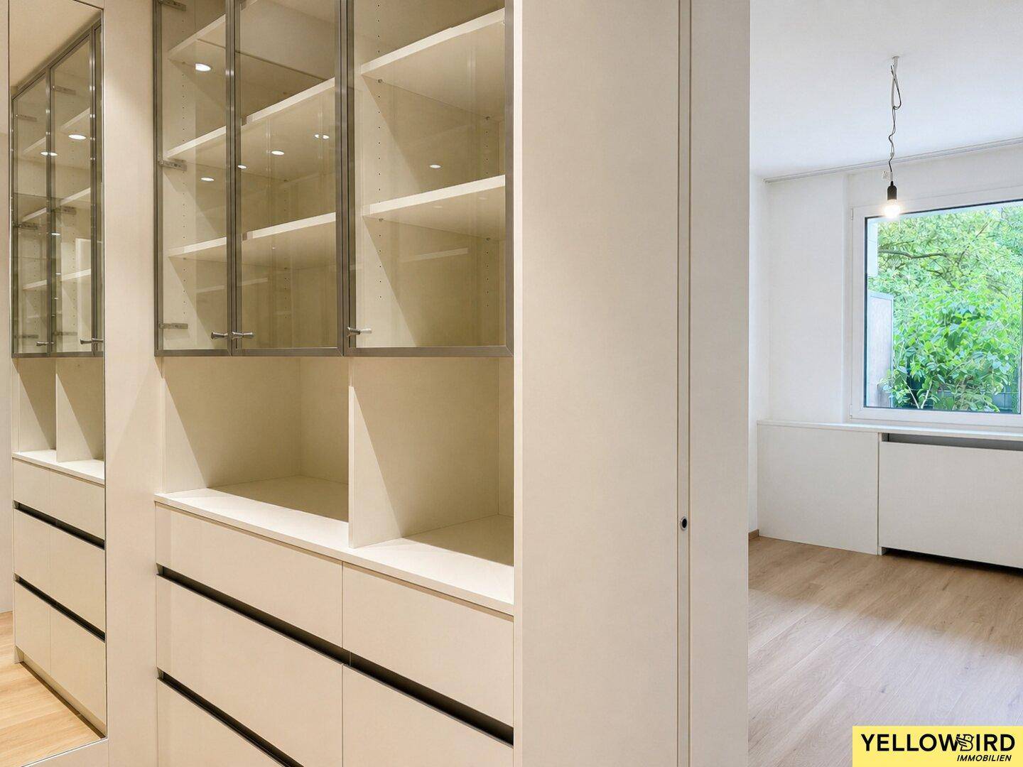 Detailansicht der weißen Einbauschränke mit Glasfronten und Blick in den begehbaren Kleiderschrank.