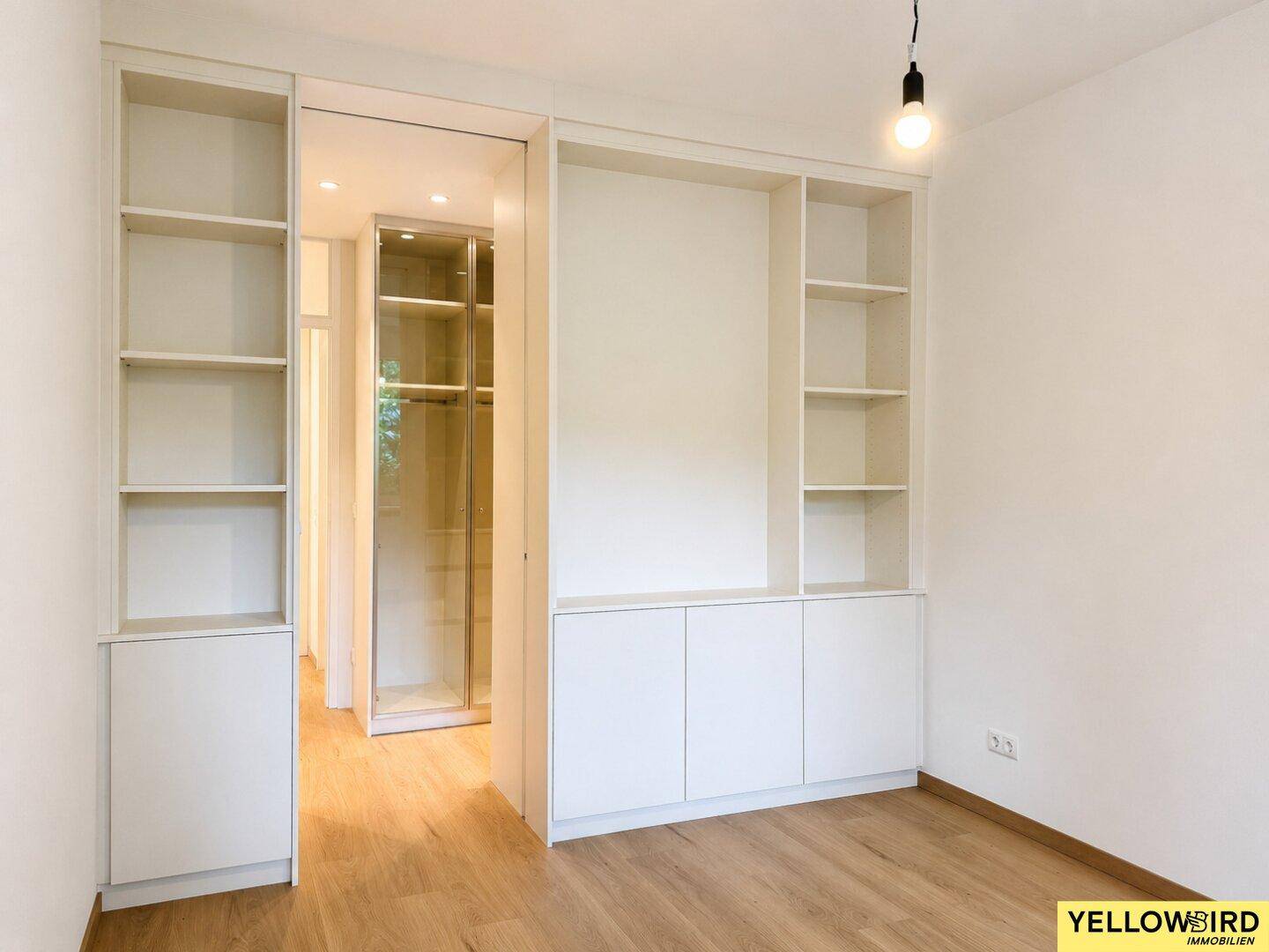 Schlafzimmer mit eleganten weißen Einbauschränken und direktem Zugang zu einem begehbaren Kleiderschrank.