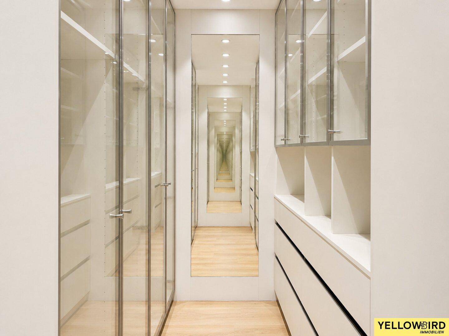 Geräumiger begehbarer Kleiderschrank mit Spiegelfronten und eleganten Glasvitrinen.