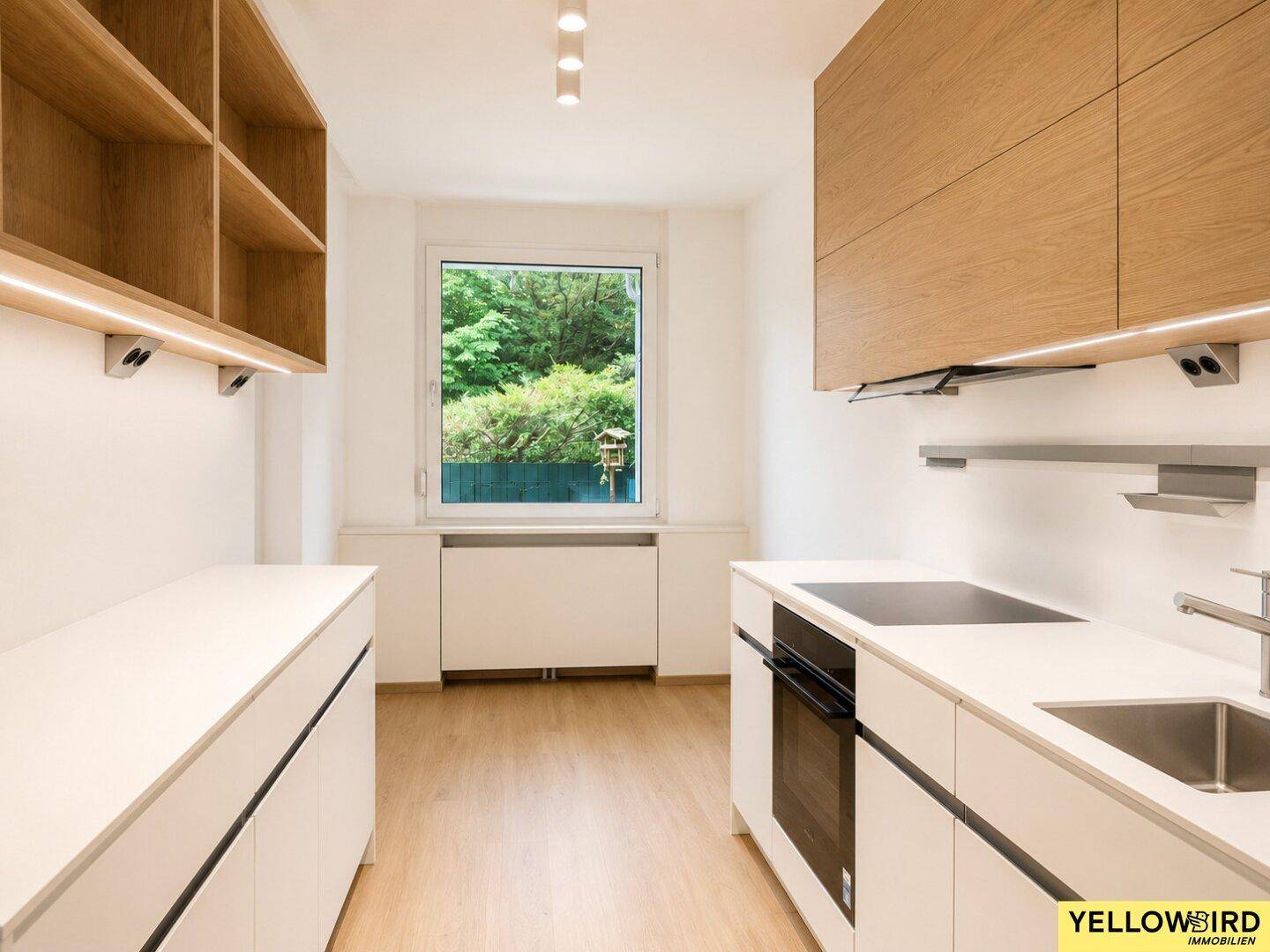 Helle Küche mit Fenster und Blick ins Grüne, ausgestattet mit modernen Einbauschränken.