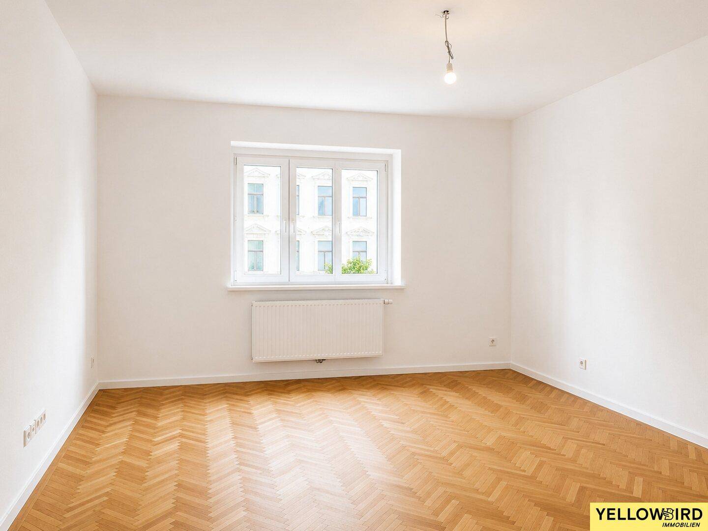 Leeres Zimmer mit klassischem Fischgrätparkett und Blick auf gegenüberliegende Gebäude.