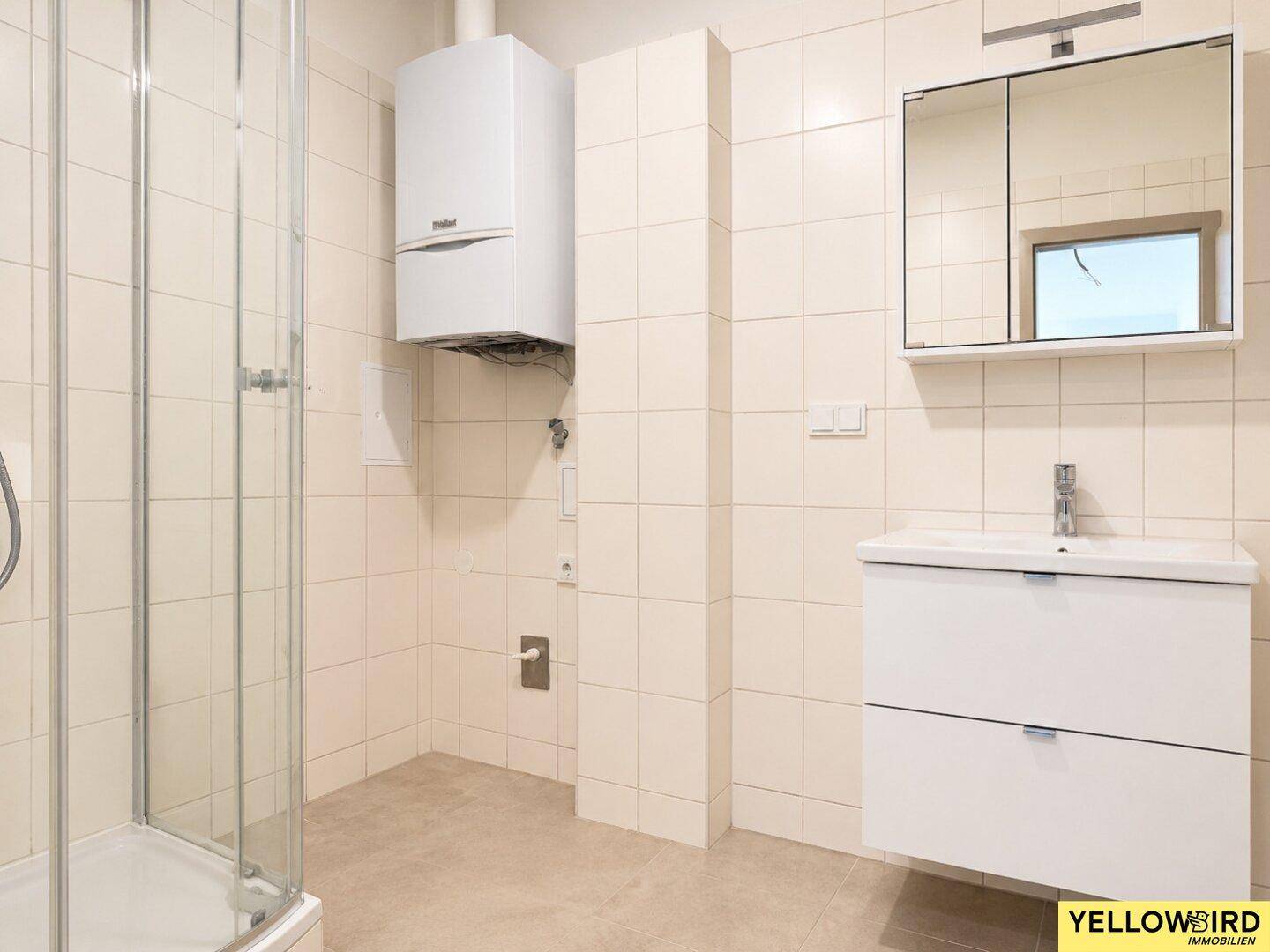 Helles Badezimmer mit Duschkabine, Waschbeckenunterschrank und Wandspiegel.