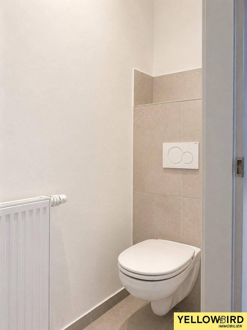 Modernes Gäste-WC mit wandhängender Toilette und beigefarbenen Fliesen.