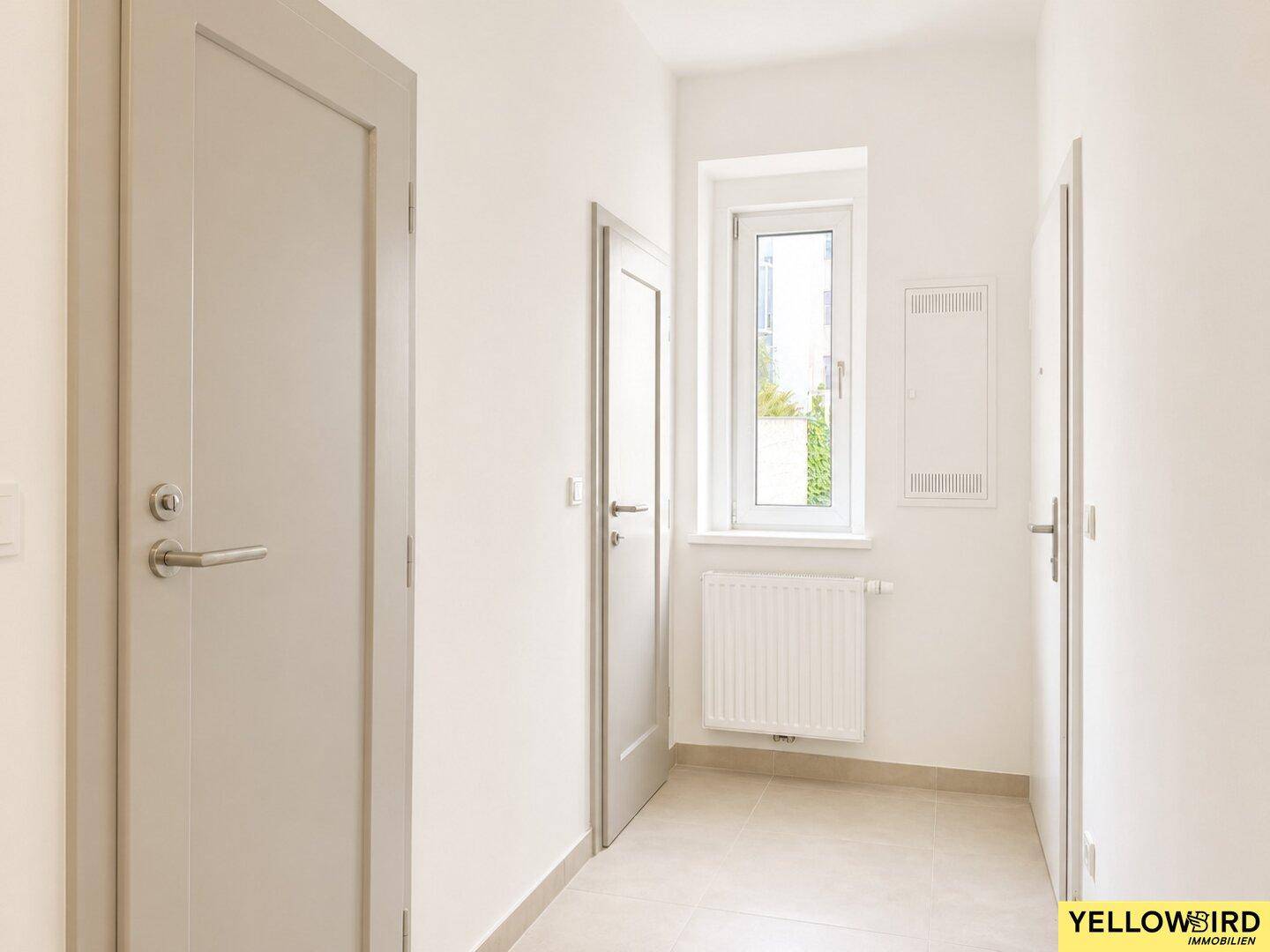 Geräumiger Flur mit mehreren Türen, Fenster und hellem Fliesenboden.