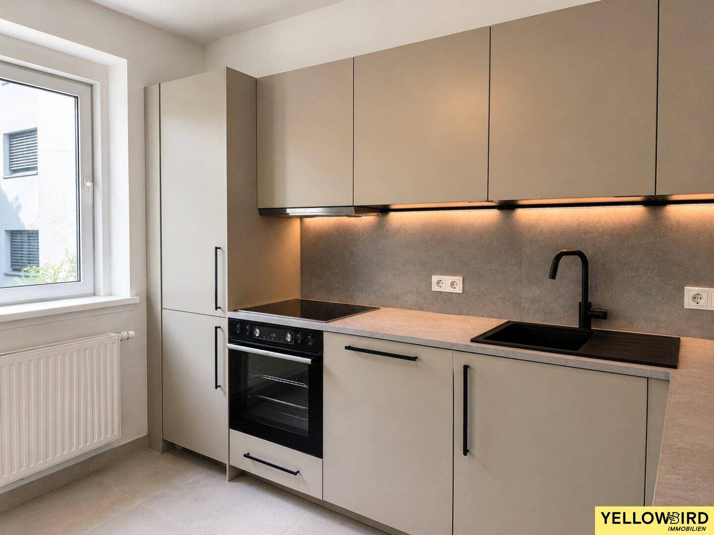 Moderne Einbauküche in Beige mit schwarzen Griffen und integrierten Geräten.