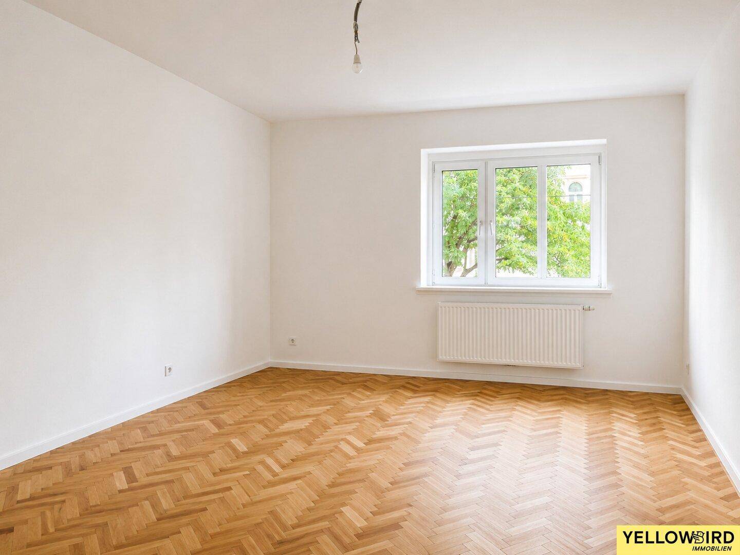 Helles Zimmer mit Fischgrätparkett und Blick ins Grüne.