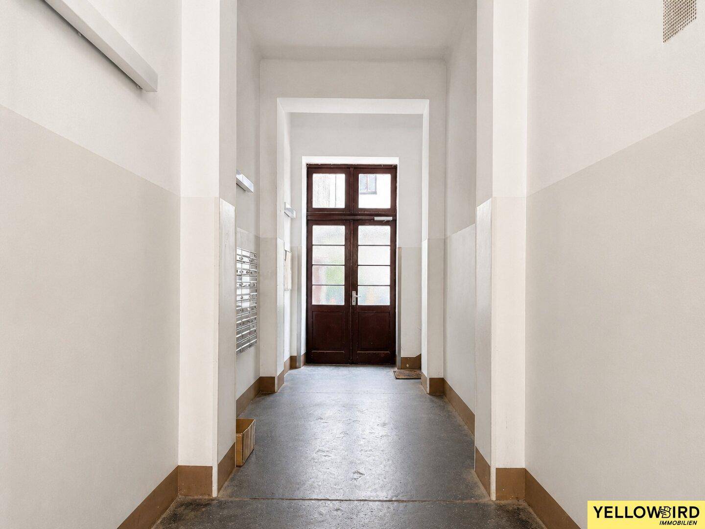 Langer, heller Hausflur mit historischer Eingangstür, der zum Treppenhaus führt.