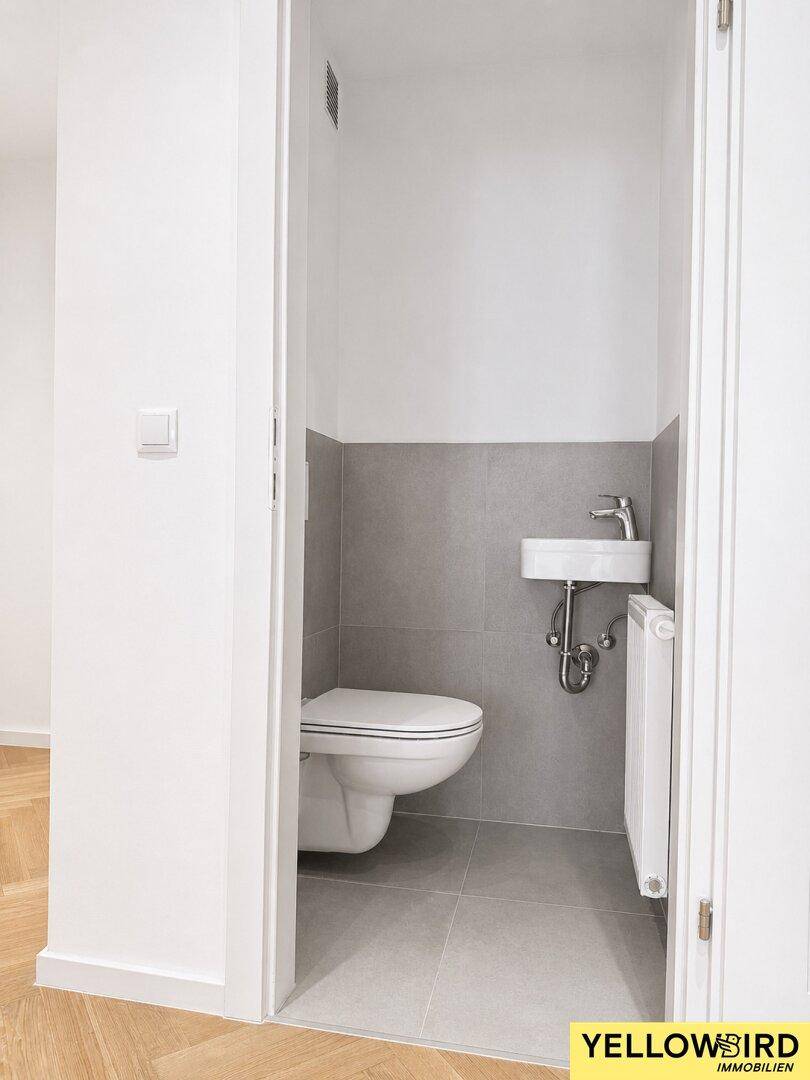 Separate Gästetoilette mit Wand-WC und kleinem Handwaschbecken, modern gefliest.