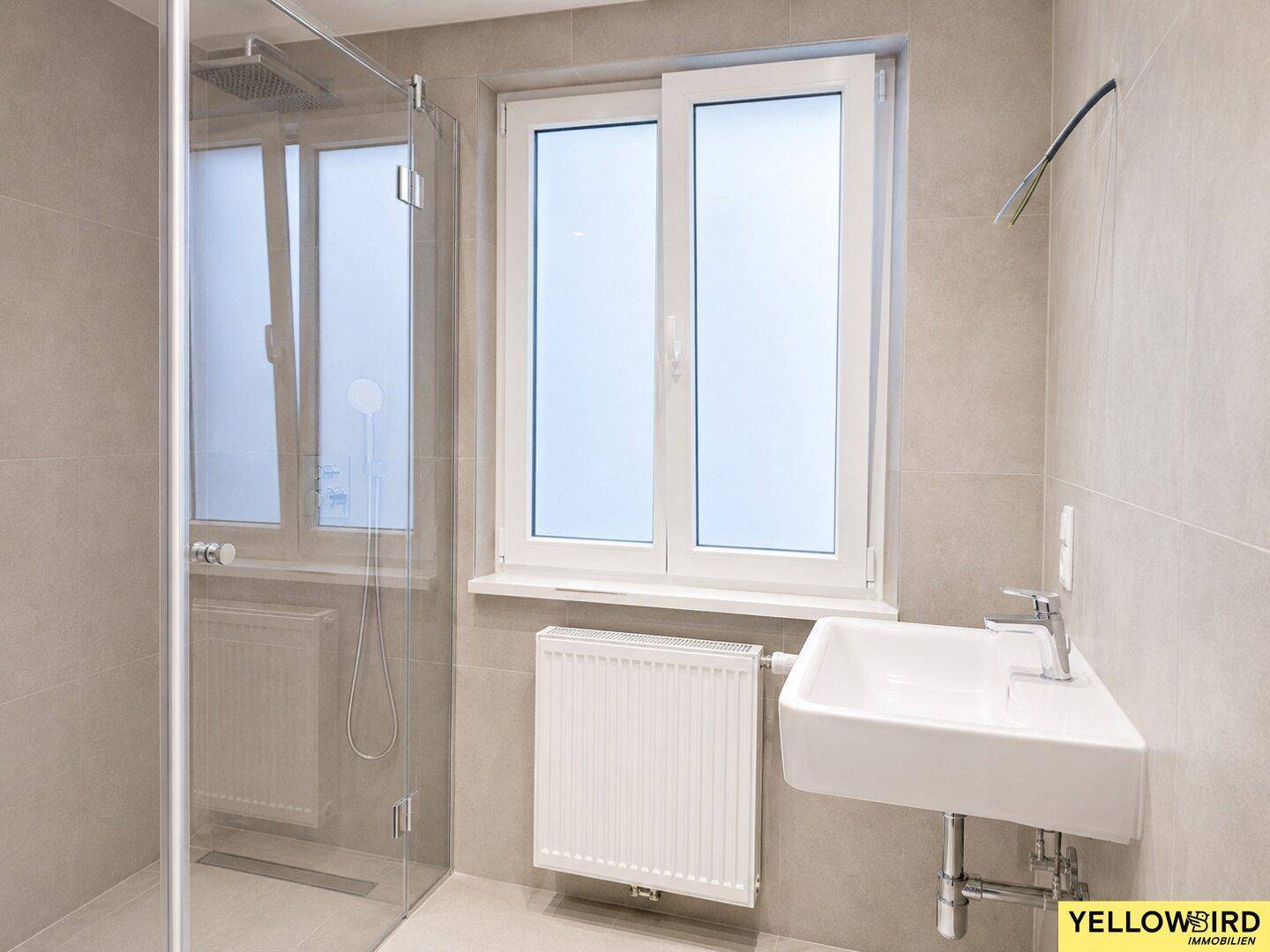 Modernes Badezimmer mit Dusche, Waschbecken und Fenster, ausgestattet mit grauen Fliesen.