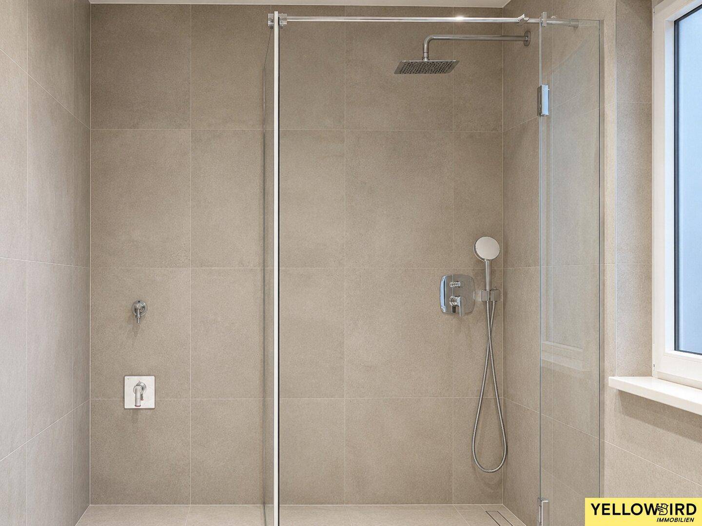 Geräumige, ebenerdige Dusche mit Glasabtrennung und Regenbrause in modern gefliestem Bad.