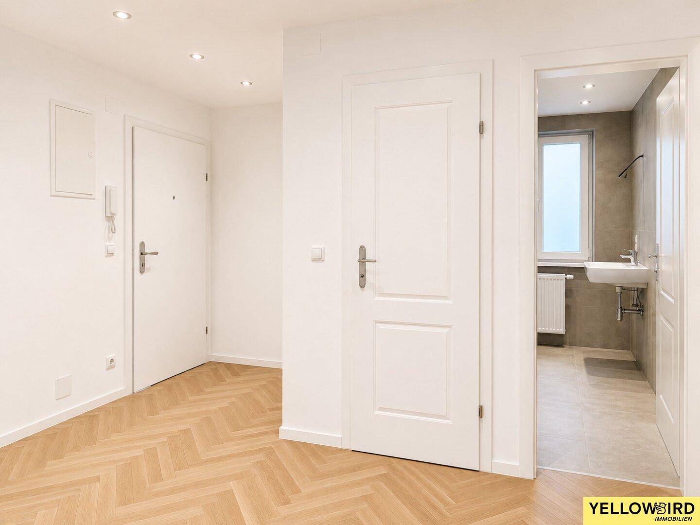 Heller Flur mit Fischgrätparkett und Zugang zu verschiedenen Räumen, inklusive Badezimmer.