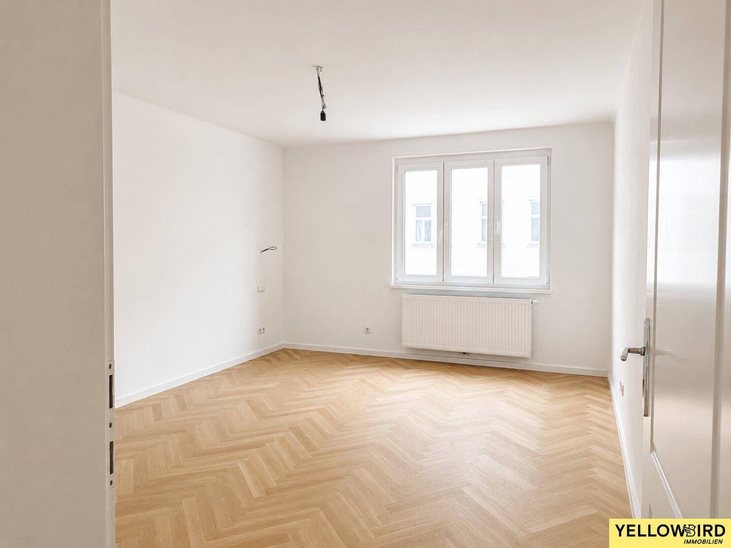 Unmöbliertes Zimmer mit hellem Fischgrätparkett und Fenster, bietet vielseitige Nutzungsmöglichkeiten.