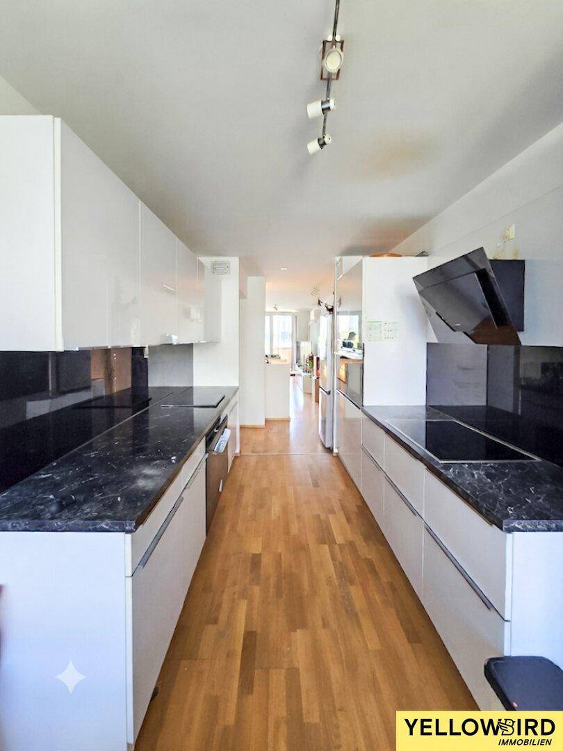 Moderne, schmale Küche mit weißen Hochglanzschränken, dunklen Arbeitsplatten und Holzboden.