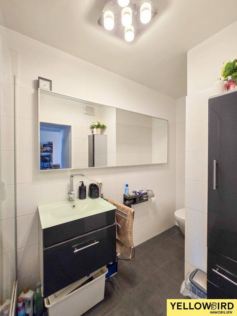 Modernes Badezimmer mit Einzelwaschbecken, großem Spiegel und dunklen Bodenfliesen.