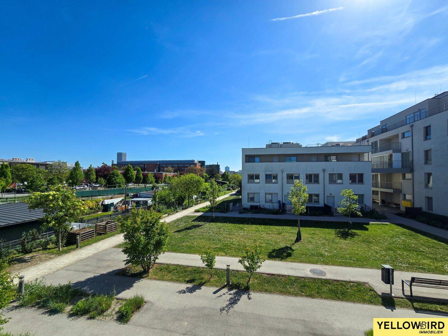 Weitläufige Grünflächen und moderne Wohngebäude unter strahlend blauem Himmel in der Umgebung.