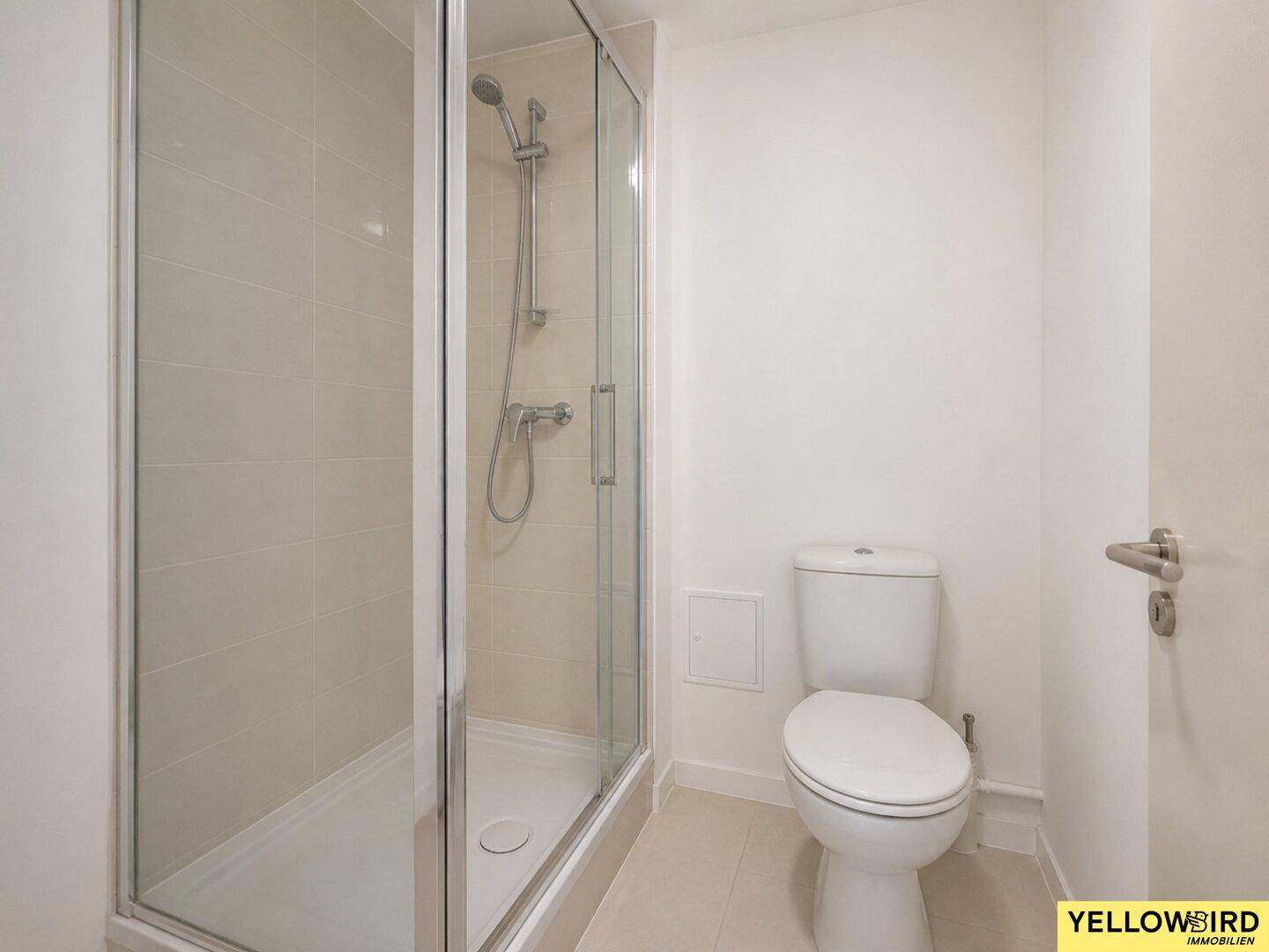 Modernes Badezimmer mit Duschkabine, WC und hellen Fliesen.