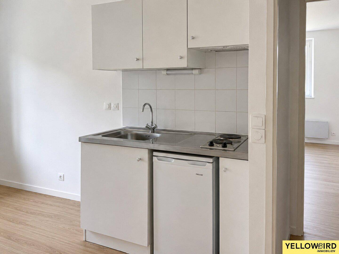 Kompakte Küchenzeile mit Spüle, Kochfeld und Kühlschrank in weißem Design.