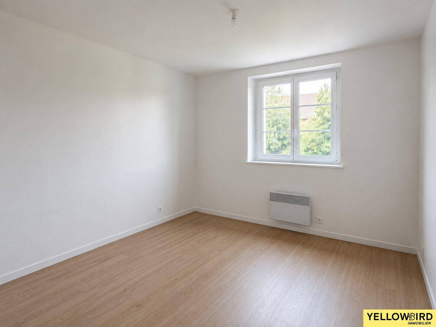 Freundliches Zimmer mit Laminatboden, weiß gestrichenen Wänden und Fensterblick.