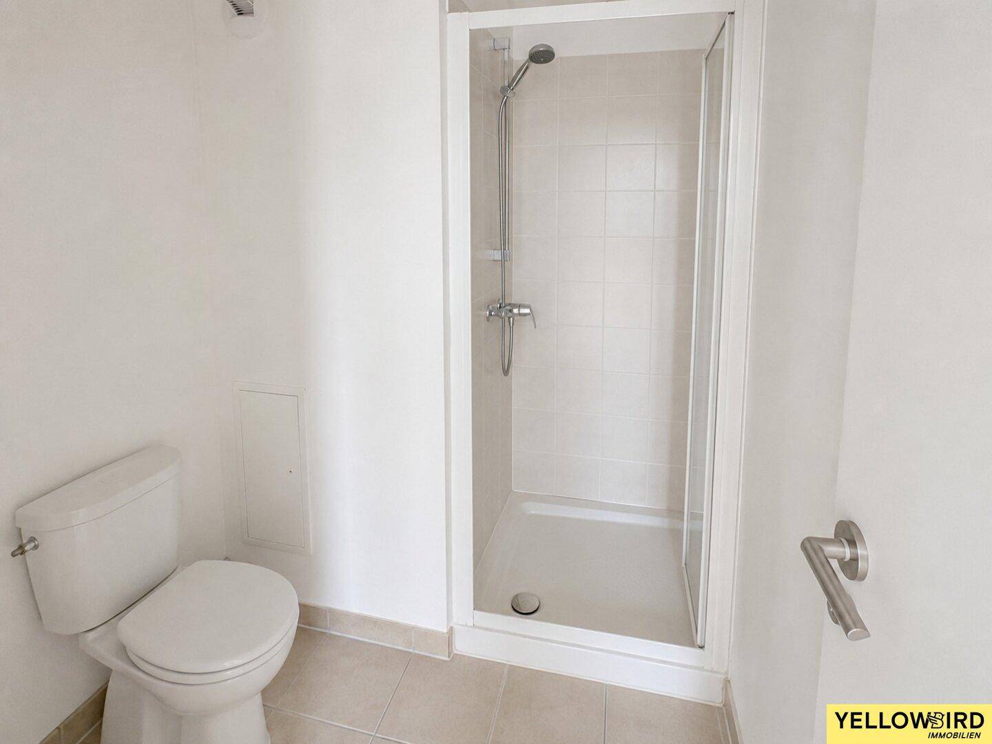 Modernes Badezimmer mit Duschkabine und WC, hell gefliest und funktional gestaltet.