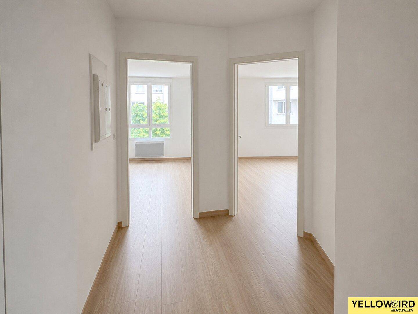 Heller Flur mit Laminatboden, der zu weiteren Zimmern mit großen Fenstern führt.