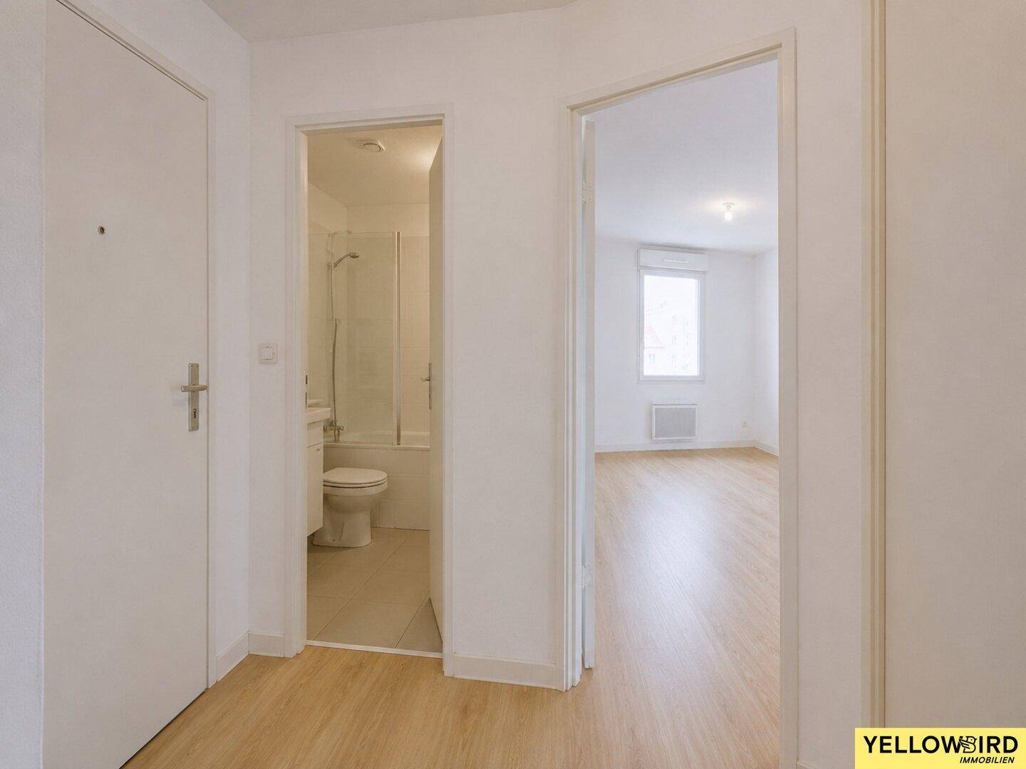 Flur mit Zugang zum Badezimmer und dem hellen Wohnbereich, ausgestattet mit Laminatboden.