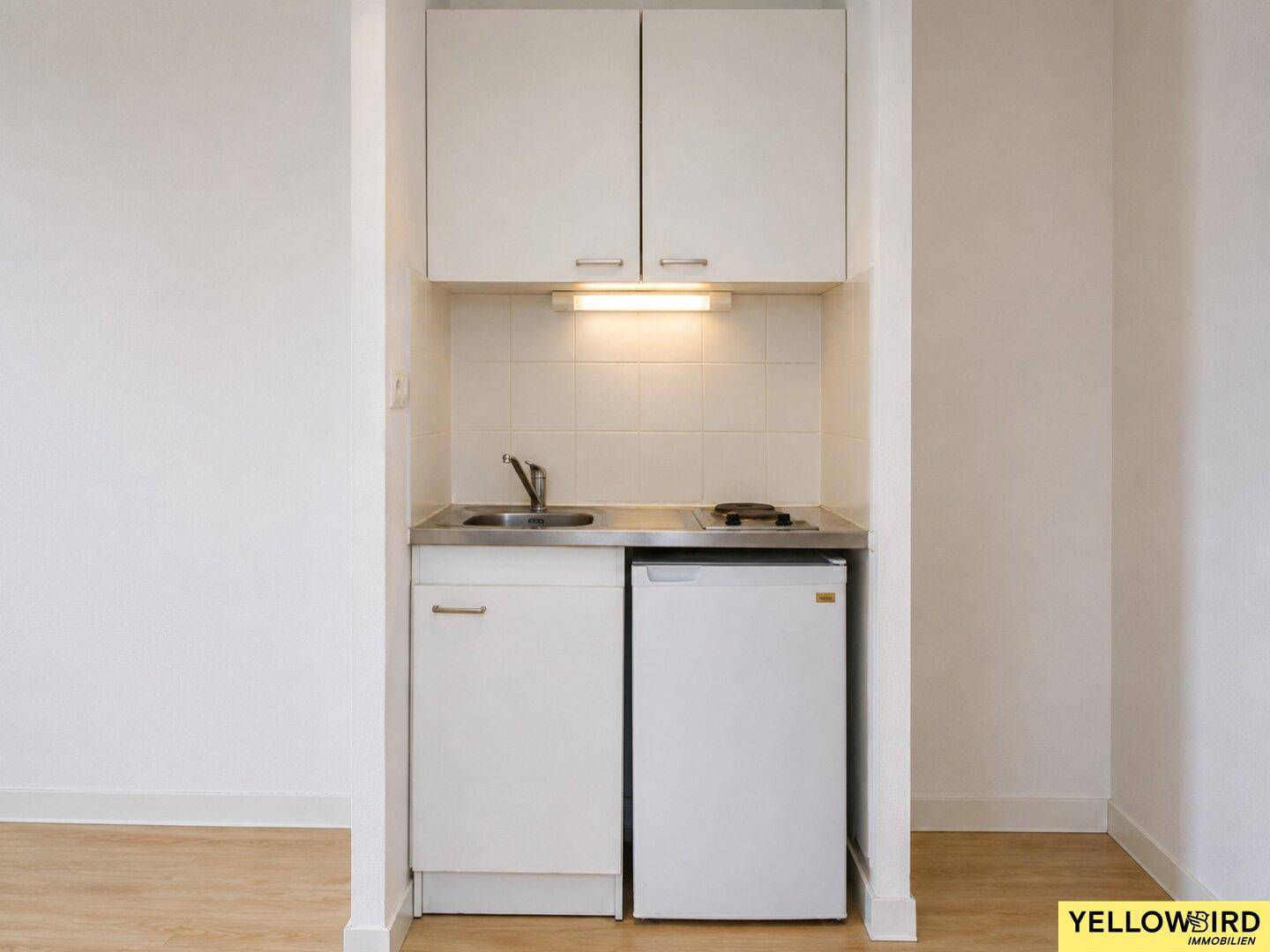 Kompakte Küchenzeile mit Spüle, Kochfeld und Kühlschrank, ideal für kleine Wohnungen.