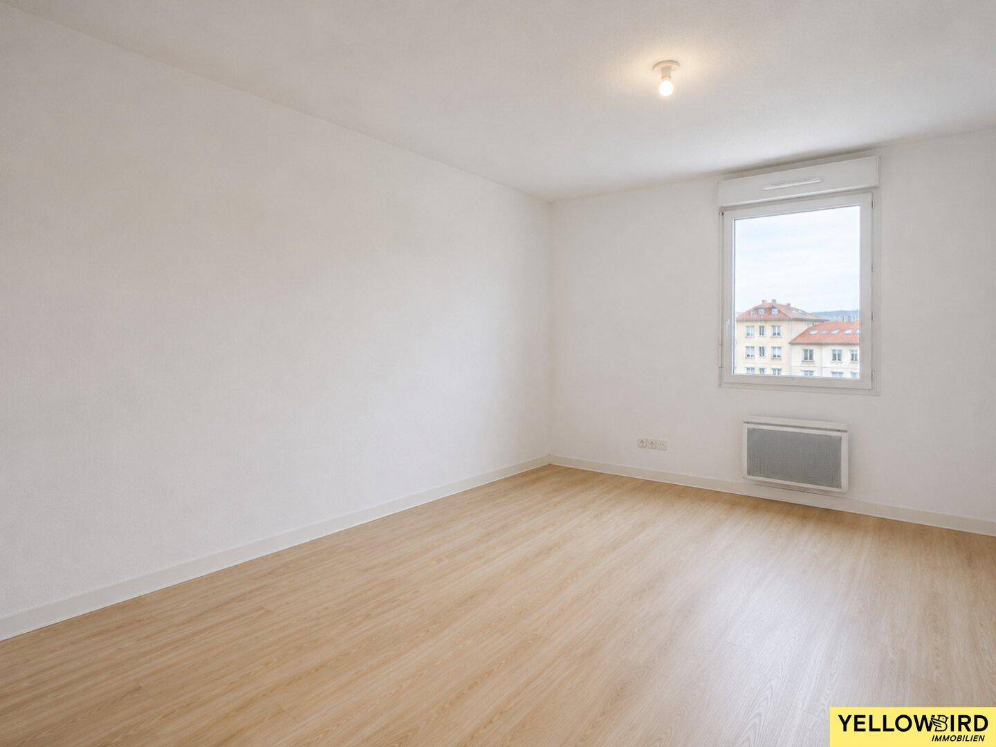 Geräumiger Wohnbereich mit hellem Laminatboden und einem Fenster, das Tageslicht hereinlässt.