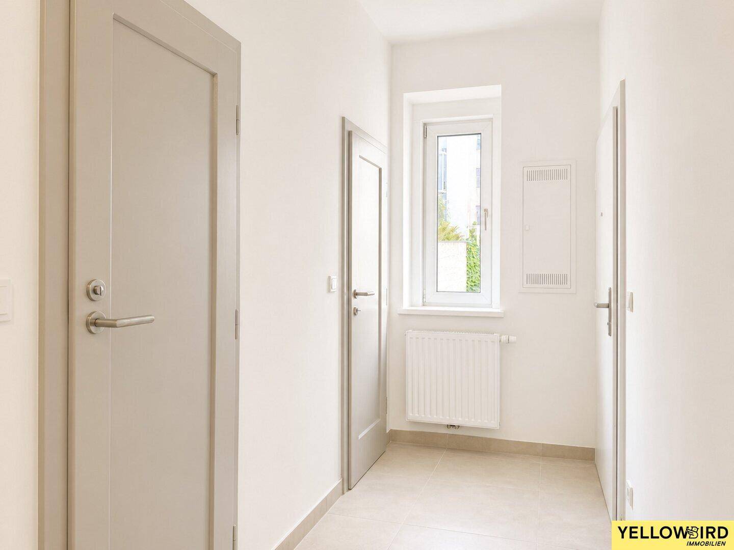 Heller Flur mit Fliesenboden, mehreren Türen und schmalem Fenster.