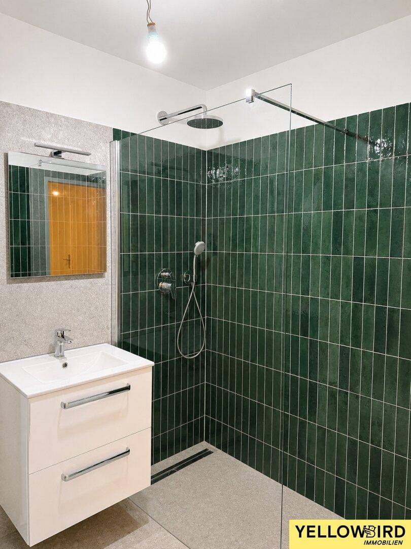 Modernes Badezimmer mit großer begehbarer Dusche, grünen Fliesen und einem eleganten Waschtisch.