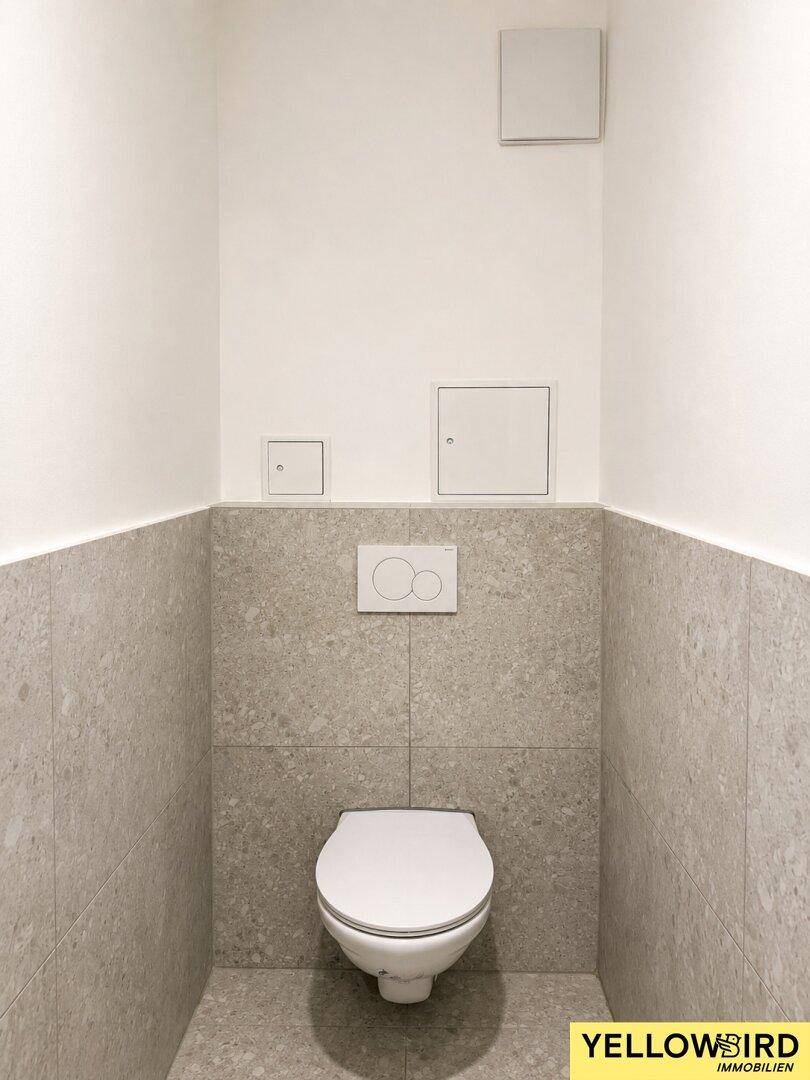 Modernes separates WC mit wandhängender Toilette und stilvollen grauen Fliesen an Wänden und Boden.