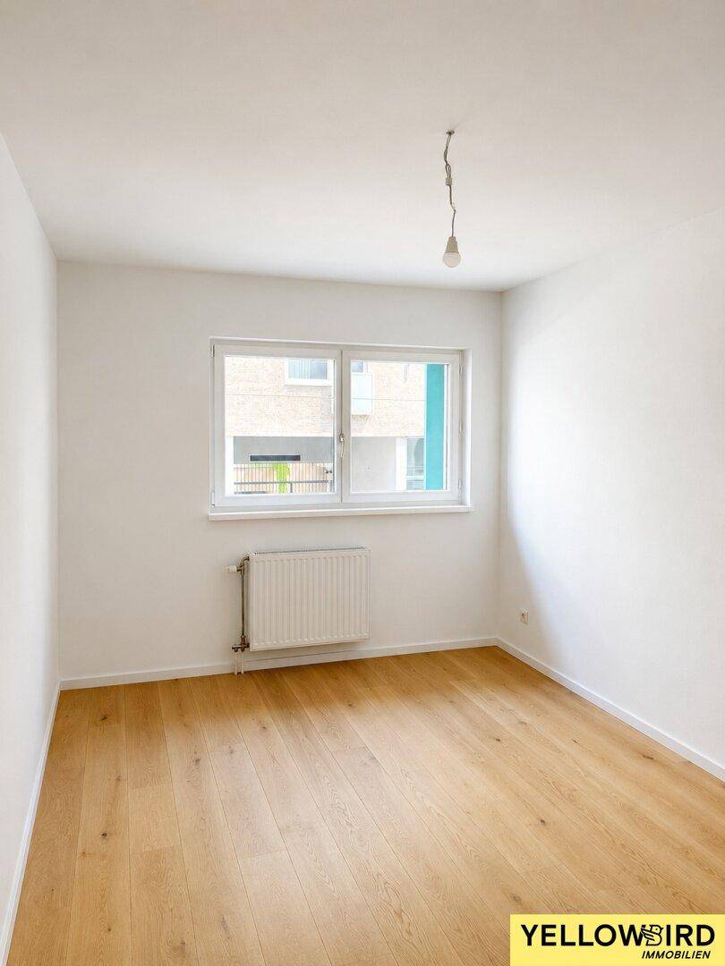 Ein weiterer heller, leerer Raum mit Parkettboden und einem Fenster, das auf moderne Gebäude blickt.
