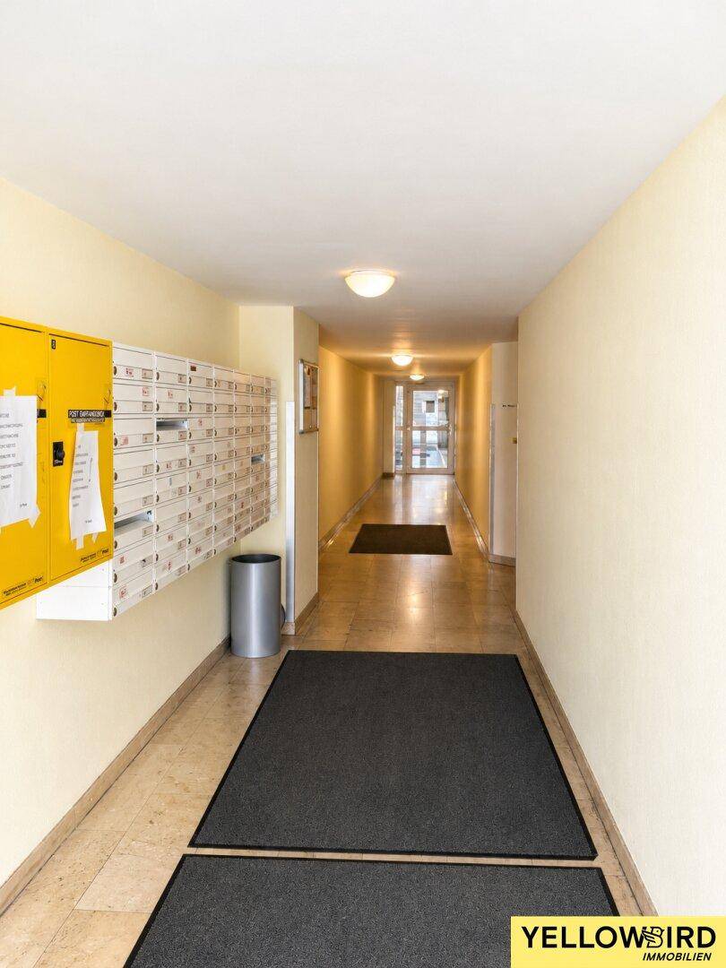 Langer, heller Flur im Eingangsbereich eines Gebäudes mit Briefkästen und gefliestem Boden.