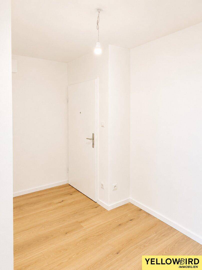 Eingangsbereich oder kleiner Flur mit heller Holzboden und weiß gestrichenen Wänden, inklusive Eingangstür.