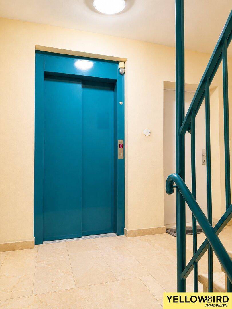 Nahaufnahme des blauen Aufzugs in einem gepflegten Treppenhaus, der Zugang zu allen Etagen bietet.