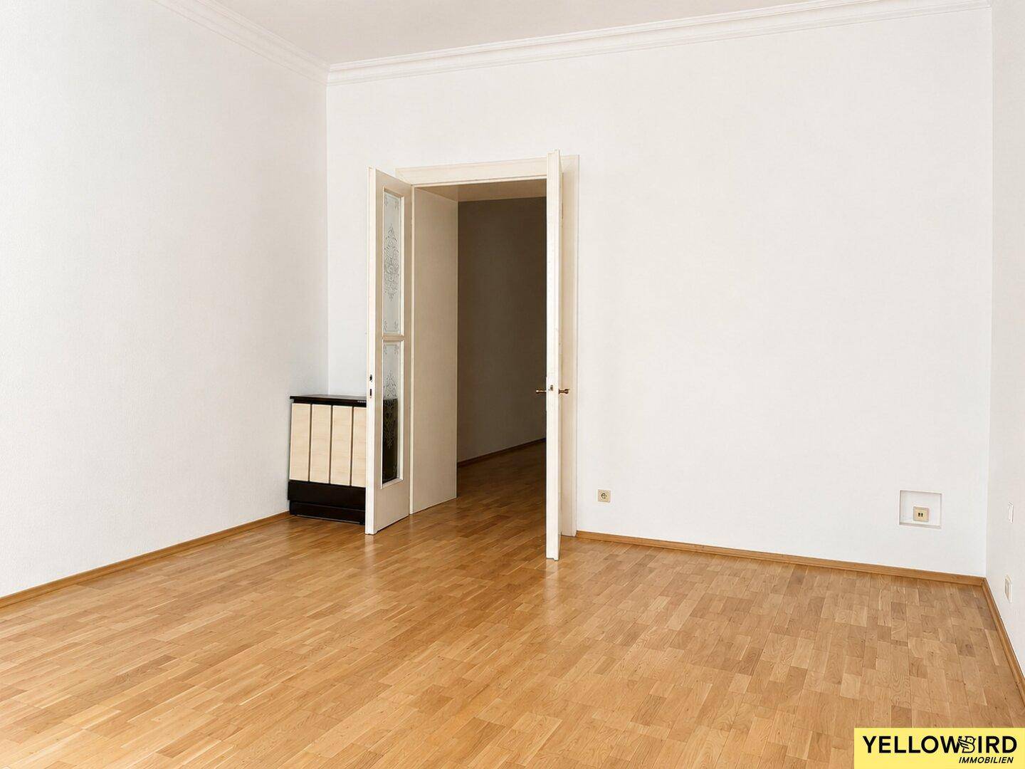 Geräumiges Zimmer mit Parkettboden, weiß gestrichenen Wänden und einer offenen Tür.