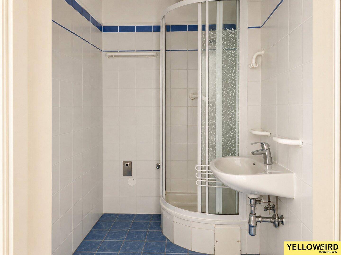 Kleines Badezimmer mit blauen Fliesen, Duschkabine und einem Waschbecken.