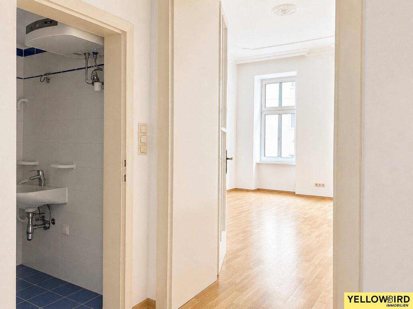 Flur mit Blick in ein helles Zimmer und ein kleines Badezimmer mit Dusche.