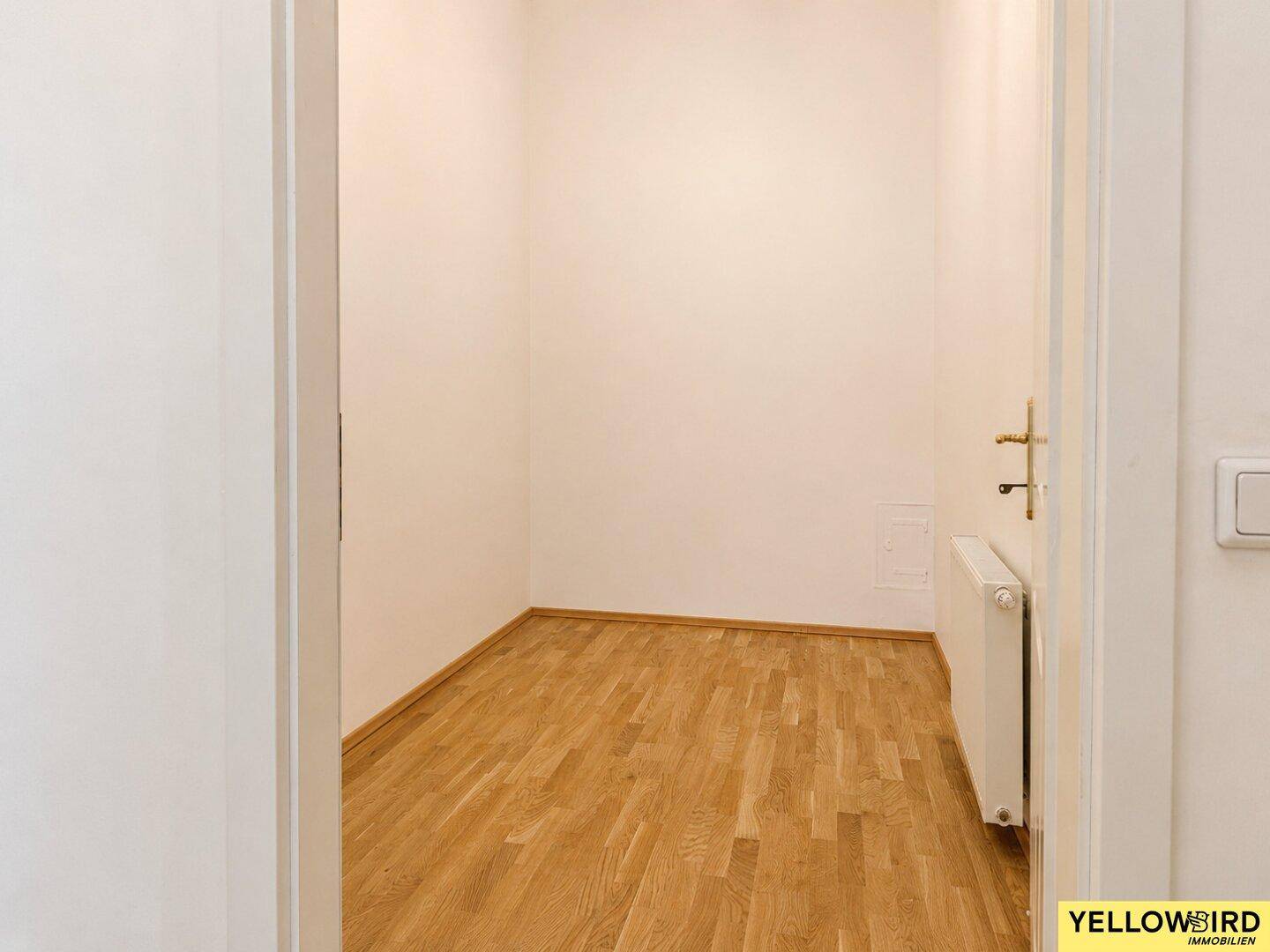 Kleiner, leerer Raum mit Parkettboden und Heizkörper, vielseitig nutzbar.