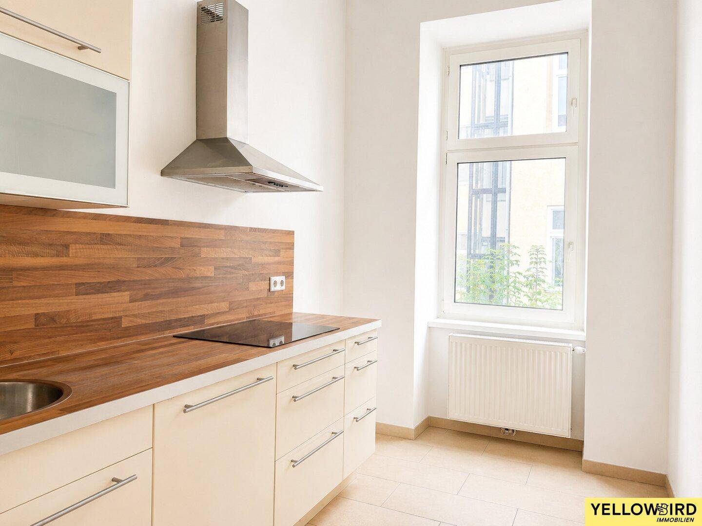 Helle Küche mit Fenster, Holzoptik-Arbeitsplatte und Dunstabzugshaube, bereit zur Nutzung.