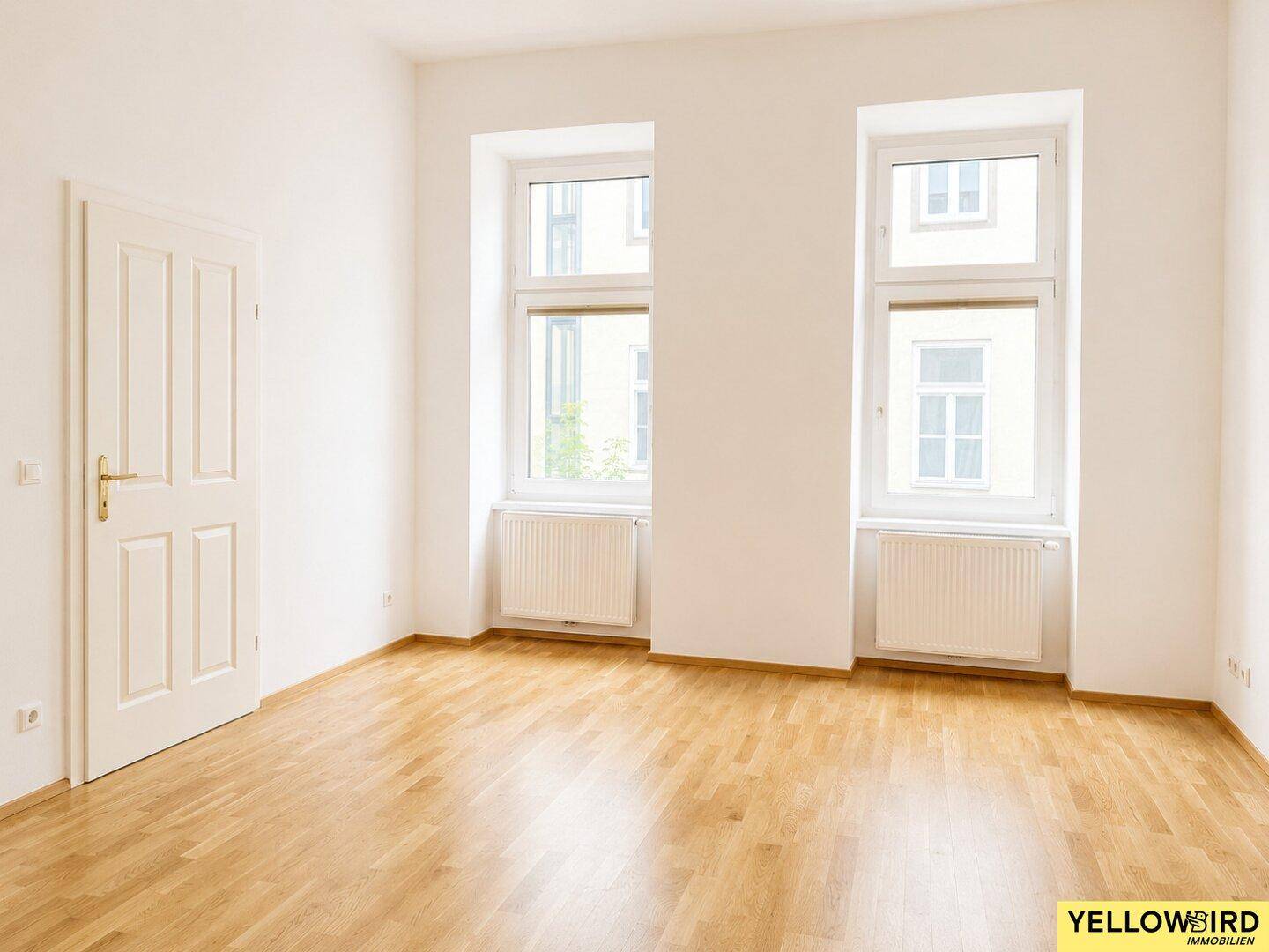 Geräumiges Zimmer mit hellem Parkettboden und hohen Fenstern, ideal für Wohnzwecke.