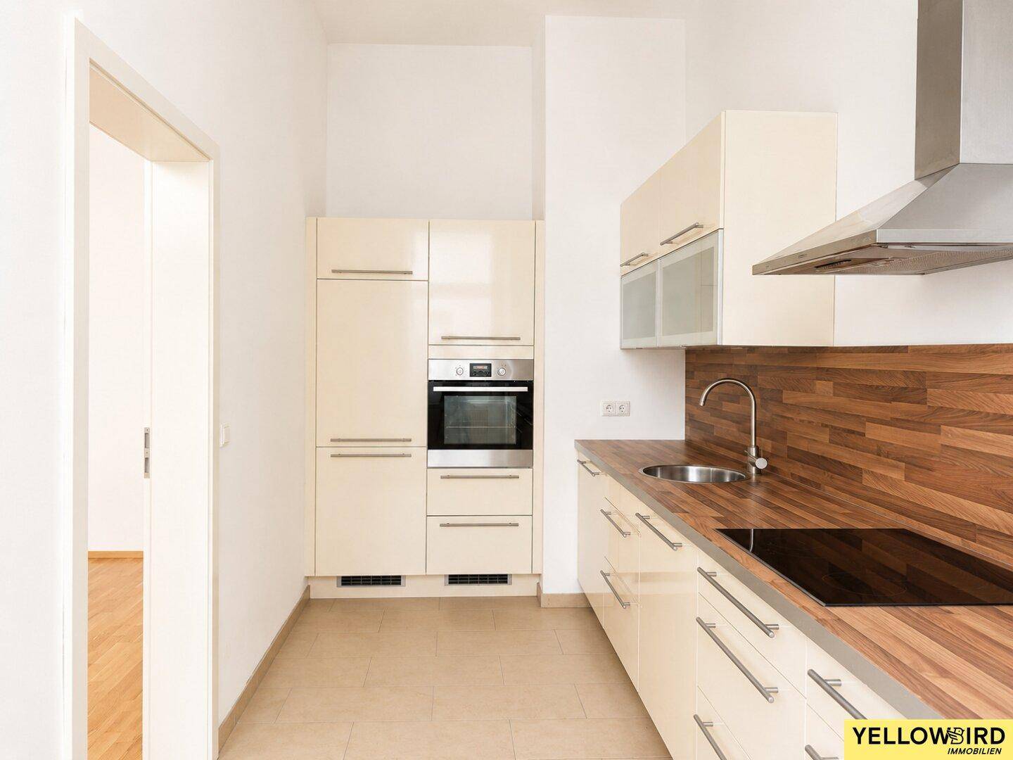 Moderne Einbauküche mit beigen Fronten, Holzoptik-Arbeitsplatte und integriertem Backofen.