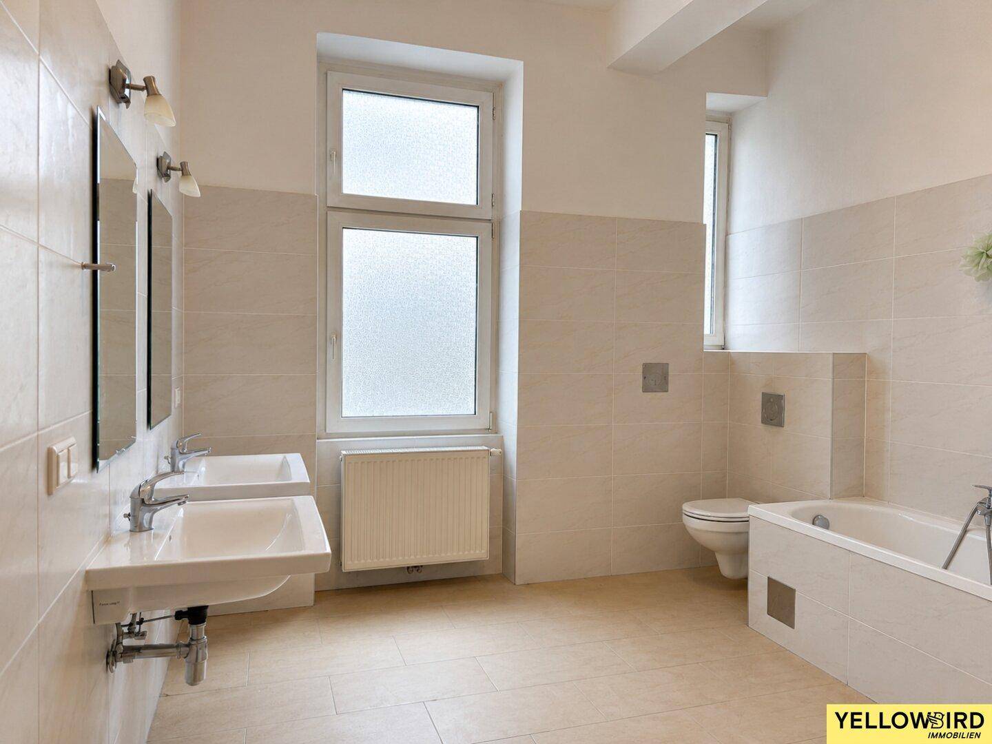 Geräumiges Badezimmer mit Doppelwaschbecken, Badewanne und Fenster für Tageslicht.